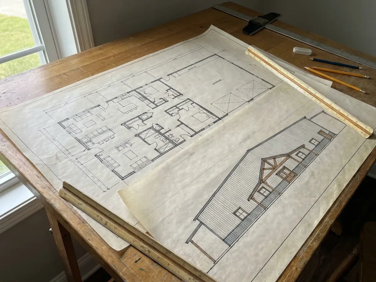 Barndominium floor plan and elevation drawings laid out on a drafting table with a scale rule.