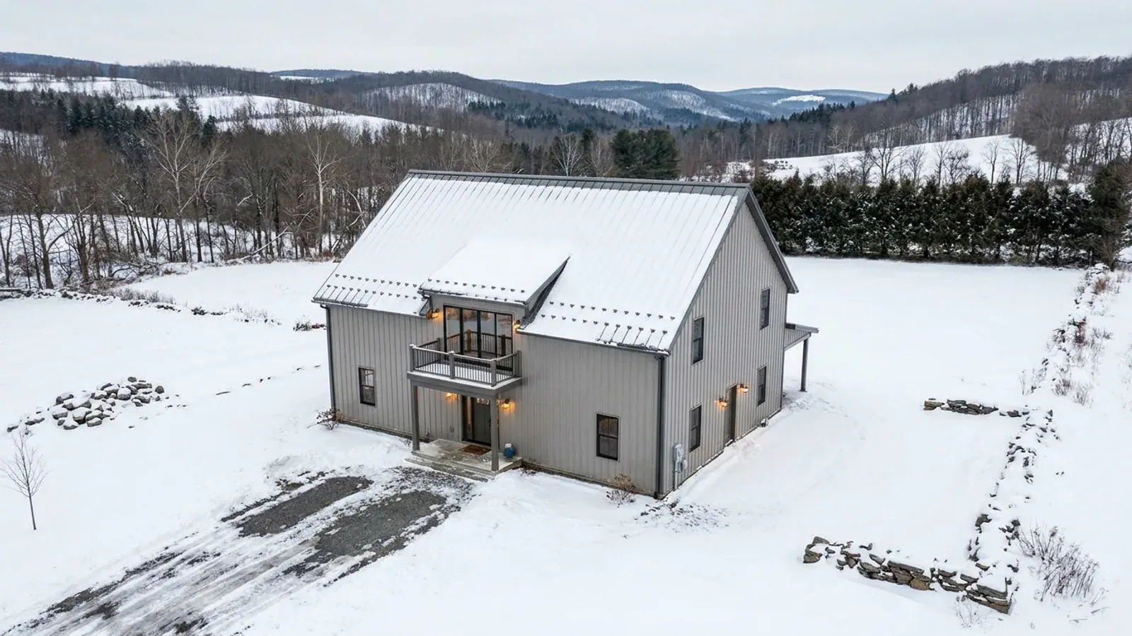 A completed two-story barndominium in winter with snow on its steep roof, second-story windows and a small covered balcony above the entry porch.